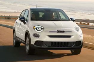 A white Fiat compact SUV drives along a coastal road, with sandy beaches and rolling hills in the background, highlighting its stylish design and scenic driving experience.