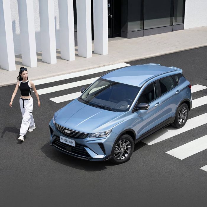 A light blue SUV parked on a crosswalk with a woman walking nearby and a modern building in the background.
