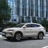 A beige BYD Song PLUS DM-i SUV on an urban road, with a modern glass building and trees in the background, showcasing its sleek design and urban appeal.