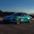 Turquoise Xiaomi SU7 parked on a road with mountains in the background.