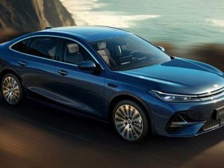 A blue Geely Galaxy A7 sedan driving on a coastal road, with the ocean and cliffs in the background, showcasing its sleek design and dynamic performance.
