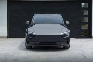 Front view of a sleek black electric SUV parked in a driveway, connected to a home charging station, with a modern garage and landscaped area, embodying eco-friendly and minimalist design.