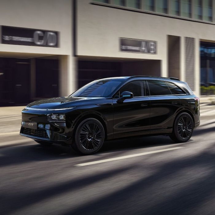A black Xpeng G9 SUV driving on a city street with modern buildings in the background.