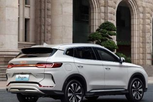Rear-side view of a white BYD Song Plus DM-i SUV, showcasing its sleek design, full-width taillights, and stylish wheels, parked on a road in front of a grand stone building.
