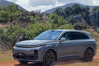 A gray Li Auto L7 driving on a dirt road with mountains and trees in the background.