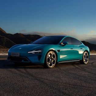 Turquoise Xiaomi SU7 parked on a road with mountains in the background.