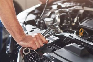 Mechanic's hand using a wrench to work on a car engine, performing maintenance, repair, or diagnostic service in an auto shop.