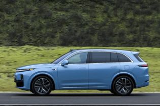 A light blue SUV driving on a road with a lush green mountain in the background.
