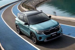 A blue Kia Seltos SUV driving on a curved road by the water.