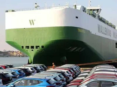 A large green and white Wallenius Wilhelmsen ship docked at a port with many cars parked nearby.