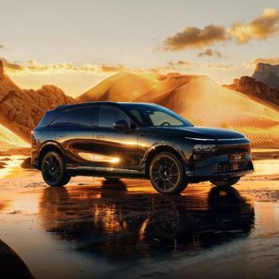 A black Xpeng G9 SUV parked in a desert landscape at sunset, with golden sand dunes and a reflective wet ground.