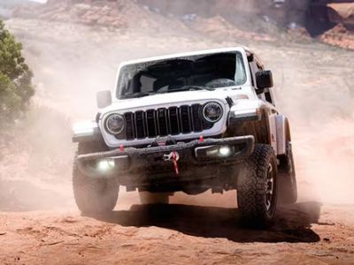 Front view of a white 2026 Jeep Wrangler driving in the sand