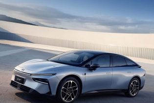 A silver Xpeng P7+ electric car parked on a paved area with a clear blue sky and distant mountains in the background.