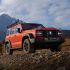A red off - road SUV parked on a rocky mountain terrain with snow - capped mountains in the background.