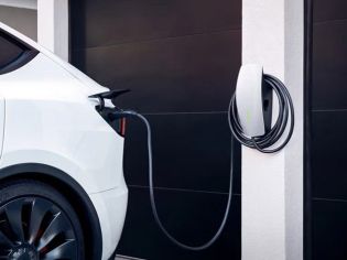White electric vehicle charging at a sleek, wall-mounted home charging station next to a dark garage door.