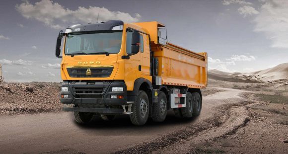 A yellow HOWO dump truck on a rugged dirt road, with a desert - like landscape and cloudy sky in the background.