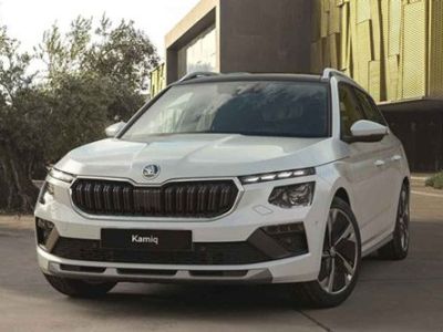White Skoda Kamiq SUV (front view) parked near a modern building with yellow facade and olive trees. Displays the Skoda logo and "Kamiq" badge on the grille.