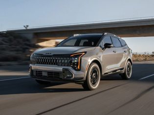 Silver Kia SUV driving on a desert highway, showcasing its bold front grille and modern design against an overpass backdrop.