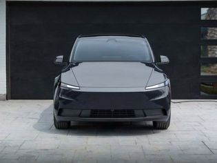 Front view of a sleek black electric SUV parked in a driveway, connected to a home charging station, with a modern garage and landscaped area, embodying eco-friendly and minimalist design.