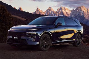 A dark - colored Xpeng G9 SUV parked with a stunning mountain range and a colorful sunset sky in the background.