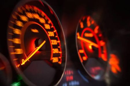 Close-up of a car's illuminated dashboard, featuring a glowing speedometer and tachometer with red/orange backlighting, capturing the thrill of high-speed driving.