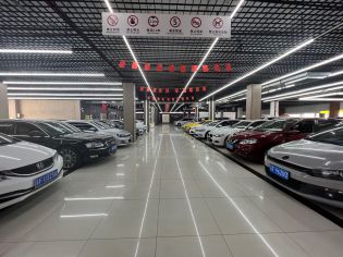 A neatly arranged car showroom with various cars parked in rows, safety signs hanging from the ceiling, and red flags decorating the space.