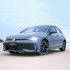A gray Volkswagen Golf parked on a sandy area under a clear sky.