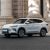 Side view of BYD Song Plus DM-i 2025 model, a light gray SUV with sleek design, parked on a road in front of a grand stone building, showcasing its elegant exterior.