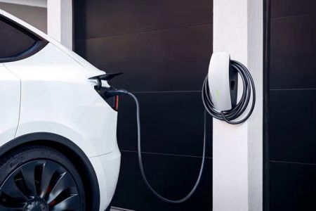 White electric vehicle charging at a sleek, wall-mounted home charging station next to a dark garage door.