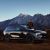 A man standing next to a black Xpeng G9 SUV, with a majestic mountain range in the background.