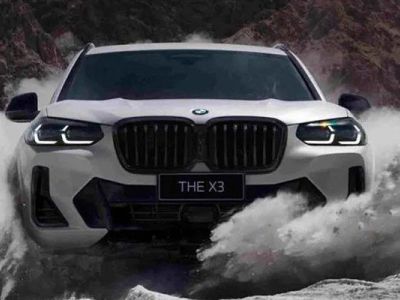 Front view of a white BMW X3 ("THE X3" badge) driving through splashing water in a rugged, mountainous area, highlighting its off-road capability and bold design.