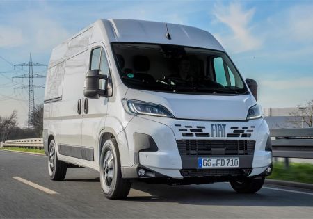 A white Fiat Ducato driving on a road under a blue sky.
