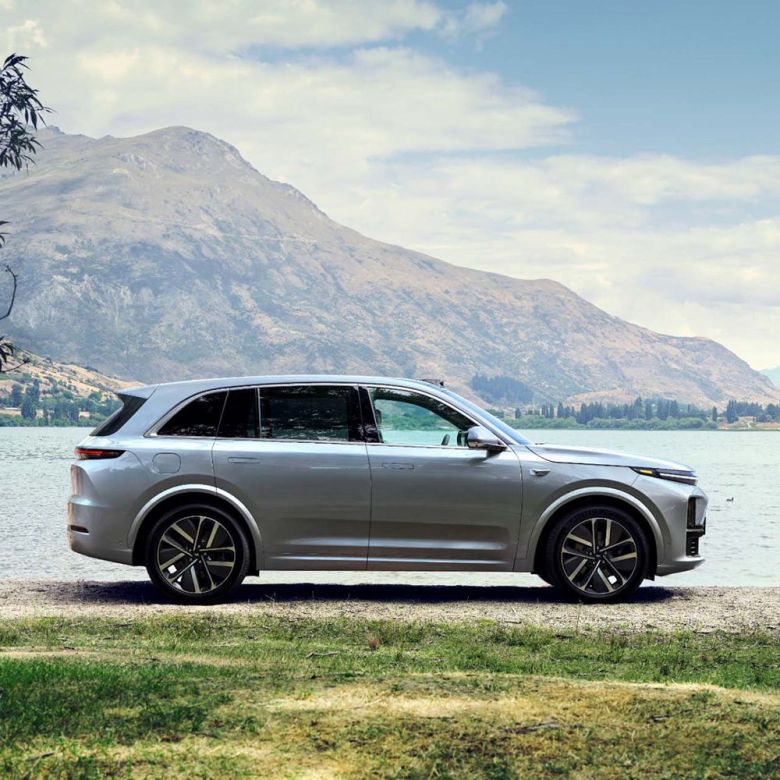 A silver SUV parked by a lake with mountains in the background.