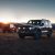 Two off - road SUVs (one gray, one red) parked on an open plain with a sunset and mountainous background.