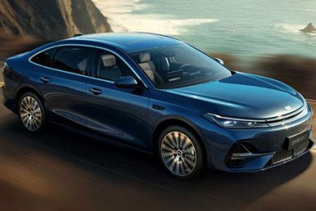 A blue Geely Galaxy A7 sedan driving on a coastal road, with the ocean and cliffs in the background, showcasing its sleek design and dynamic performance.