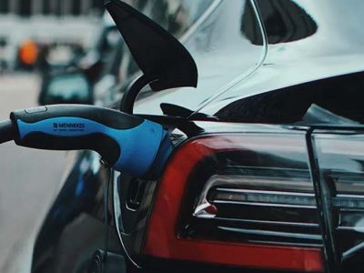 Close - up of an electric car being charged with a blue charging plug.