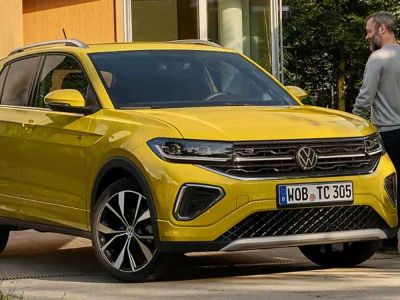Bright yellow Volkswagen SUV (with VW logo, alloy wheels) parked by a building; a man walks beside it.