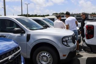 Ford Maverick pickup trucks: A group of people inspecting white Ford Mavericks at an outdoor car dealership lot.