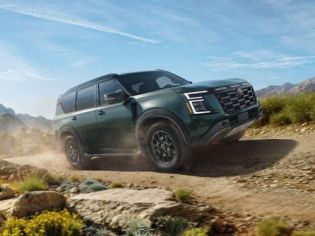 2026 Nissan Armada NISMO driving on a dirt road near some rocks and wildflowers
