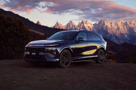 A dark blue SUV parked on a rocky terrain, with majestic mountains and a colorful sunset sky in the background, highlighting its sleek design and scenic surroundings.