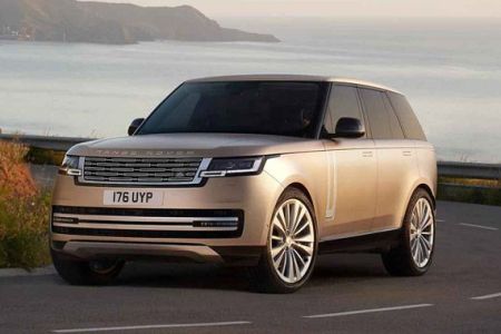 A beige Range Rover with license plate 176 UYP, parked on a coastal road with a scenic sea and mountain backdrop, showcasing luxury and adventure.