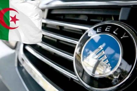 Close-up of a Geely car emblem on a grille, paired with the Algerian flag in the background, linking the automaker to Algeria.