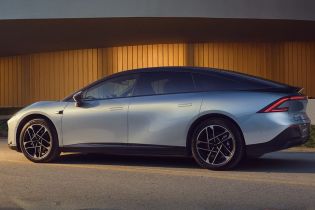 Side view of a silver electric car parked in front of a modern building with a golden facade.