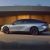 Side view of a silver electric car parked in front of a modern building with a golden facade.