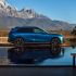A blue Xpeng electric SUV parked by a reflective body of water, with a majestic mountain range in the background.