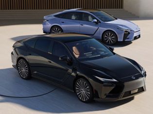 Two sleek modern electric sedans in black and light blue parked outdoors; front vehicle plugged in for charging against neutral backdrop