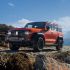 An orange off - road SUV parked on a rocky mountain terrain under a blue sky with white clouds.