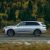 A silver SUV driving on a road with a forest in the background.