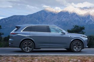 A gray SUV driving on a road with snow - capped mountains in the background.