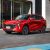 A red Forthing T5 EVO SUV with a black roof, showcasing its bold grille and sleek design, parked on a paved area in front of a modern building with large glass windows.